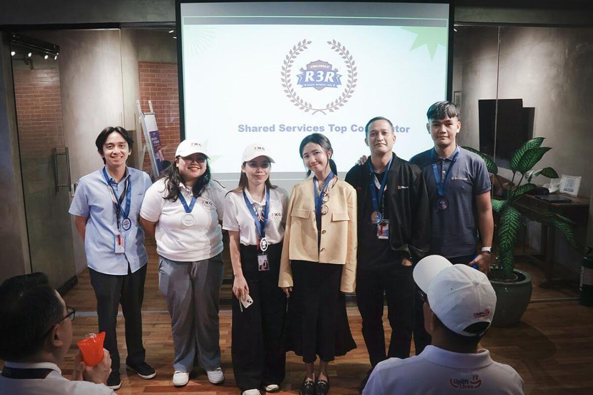 Employees posing together in front of a presentation screen at a company event